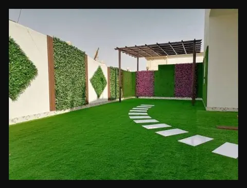 حديقة بعشب صناعي وممر بلاطات منحني وجدار عشبي