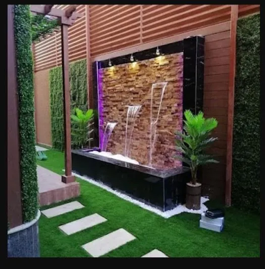 شلال بواجهة حجرية نحاسية وحوض أسود وعشب صناعي